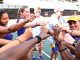 Group of diverse young athletes in a circle joining their fists for a team cheer on a track field.