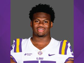 Portrait of a college football player wearing an LSU jersey (white with purple and gold) against a gray backdrop.