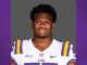 Portrait of a college football player wearing an LSU jersey (white with purple and gold) against a gray backdrop.
