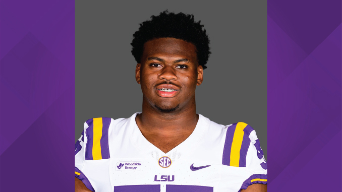 Portrait of a college football player wearing an LSU jersey (white with purple and gold) against a gray backdrop.