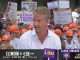 A man in a light blue shirt speaking into a headset mic in front of a crowded fan group with orange hard hats and handmade signs, on a college football broadcast overlay.