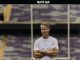 Man in a white T-shirt with arms crossed standing in an empty football stadium.