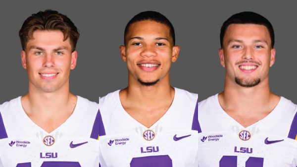 Three LSU football players in white and purple jerseys stand side by side, smiling at the camera against a gray backdrop.