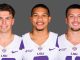 Three LSU football players in white and purple jerseys stand side by side, smiling at the camera against a gray backdrop.