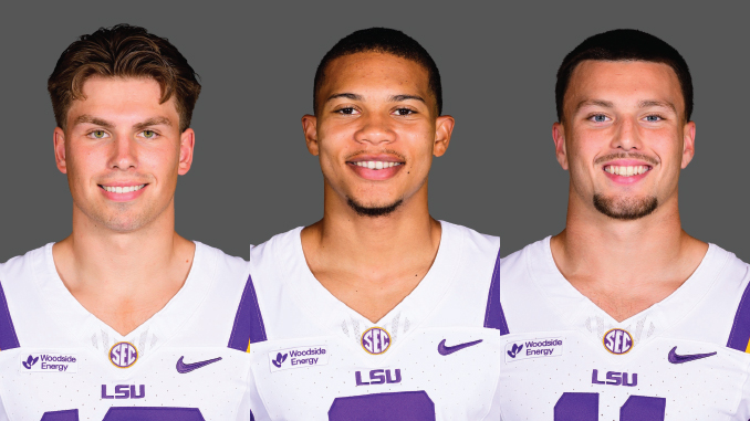 Three LSU football players in white and purple jerseys stand side by side, smiling at the camera against a gray backdrop.