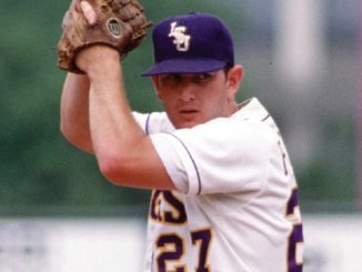 Baseball pitcher in a white uniform and dark cap, glove raised as he prepares to throw.