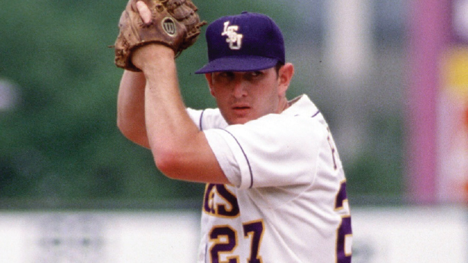 Baseball pitcher in a white uniform and dark cap, glove raised as he prepares to throw.