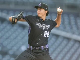 Male baseball pitcher in a black uniform with number 28, mid-throw on the mound at a stadium.