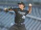 Male baseball pitcher in a black uniform with number 28, mid-throw on the mound at a stadium.