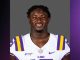 Smiling LSU football player in a purple and gold jersey (white jersey with purple/yellow stripes) posed against a gray backdrop.