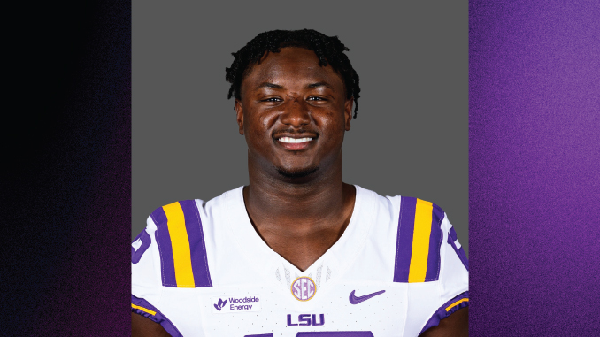 Smiling LSU football player in a purple and gold jersey (white jersey with purple/yellow stripes) posed against a gray backdrop.