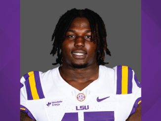 Portrait of a college football player in an LSU white jersey with purple and gold stripes, facing the camera.