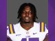 Portrait of a college football player in an LSU white jersey with purple and gold stripes, facing the camera.