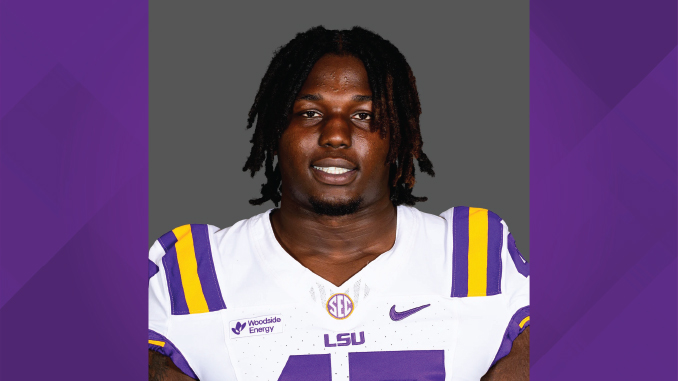 Portrait of a college football player in an LSU white jersey with purple and gold stripes, facing the camera.