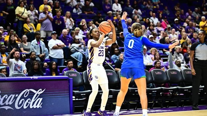 LSU player in white #23 drives with the ball while defender in blue #0 reaches in during a college basketball game with a packed crowd behind.