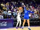 LSU player in white #23 drives with the ball while defender in blue #0 reaches in during a college basketball game with a packed crowd behind.