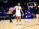 LSU women’s basketball player wearing #12 in a white jersey dribbles the ball while a defender in black guards her near the court with a referee and spectators in the background.
