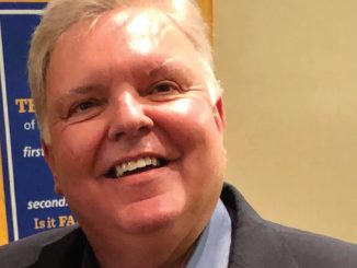 Smiling man in a dark blazer and light blue shirt, posing for the photo.