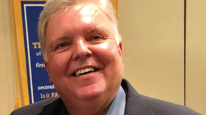 Smiling man in a dark blazer and light blue shirt, posing for the photo.