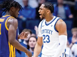 Kentucky player #23 in white jersey confronts a purple-uniform opponent during a heated basketball moment.