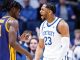 Kentucky player #23 in white jersey confronts a purple-uniform opponent during a heated basketball moment.