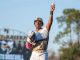 Baseball pitcher raises his arm in triumph after a strikeout on the field with a blurred stadium in the background.