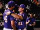 Two baseball players in purple uniforms hug on the field as fans watch in the stands, numbers 45 and 21 visible on their jerseys.