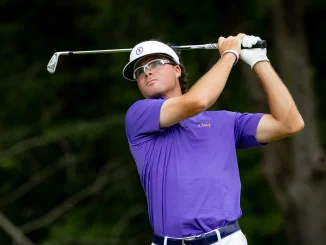 Golfer in a purple LSU polo swings a club during a backswing with a white visor and protective glasses.