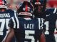 Ole Miss Rebels football players seen from the back during a game; center is LACY #5, flanked by teammates KUTAS #70 and another player #41.