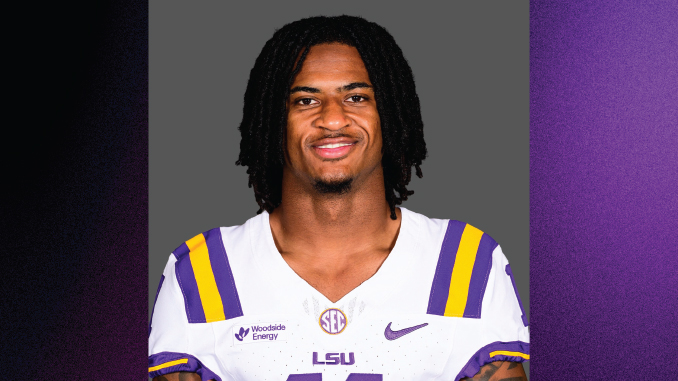 Portrait of an LSU football player with dreadlocks, wearing a white jersey with purple and gold stripes, against a gray backdrop.
