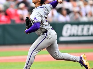 Left-handed? (Correction: right-handed) Right-handed pitcher in gray and purple throwing from the mound during a game, with crowd in background.