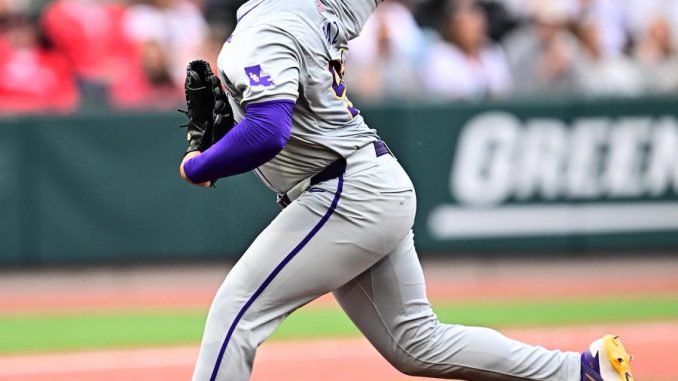 Left-handed? (Correction: right-handed) Right-handed pitcher in gray and purple throwing from the mound during a game, with crowd in background.