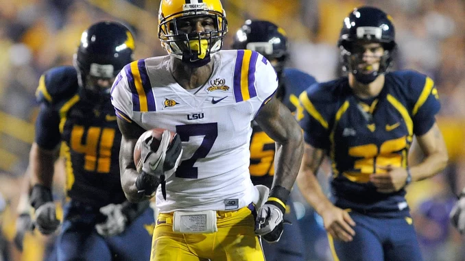 LSU football player in white and purple, wearing #7, sprints with the ball as defenders in navy and gold chase him on the field.