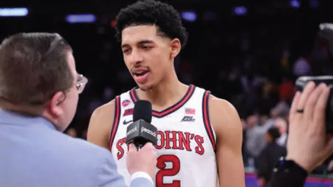 Basketball player in a St. John's jersey being interviewed on court, microphone held near his mouth, crowd in the background, jersey number 2 visible.