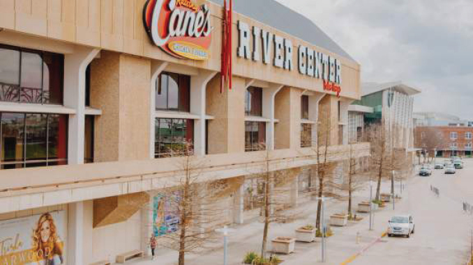 Exterior view of River Center mall with a Raising Cane's sign and a row of bare trees along the sidewalk