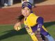Female softball pitcher in a yellow LSU uniform delivers a fast throw on the mound, ball in hand and glove extended forward.