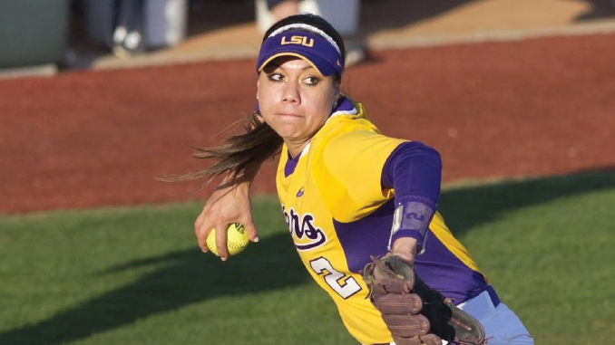 Female softball pitcher in a yellow LSU uniform delivers a fast throw on the mound, ball in hand and glove extended forward.