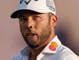 Close-up of a golfer wearing a white polo with Mastercard logo on the collar and a white cap, looking focused.