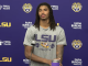 LSU football player with long dreadlocks at a press conference, wearing a gray 'LSU Strength' shirt, microphone at a podium against a purple backdrop with logos.