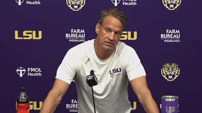 Press conference scene with LSU coach at a podium, purple backdrop featuring LSU, FMOL Health, and Farm Bureau logos; coach in white LSU shirt speaks into a microphone.