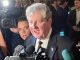 Former U.S. President Bill Clinton speaks to reporters as cameras and microphones surround him at a press event.