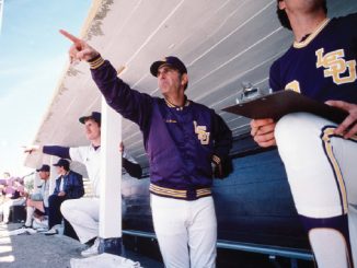 Baseball dugout scene: coach in a purple LSU jacket points toward the field as players watch.