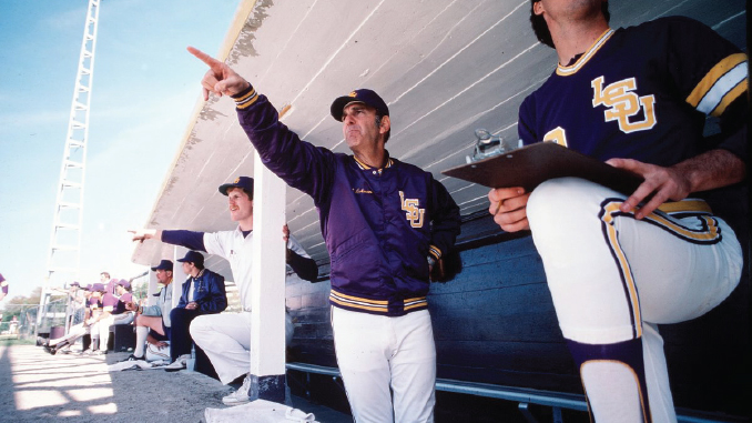 Baseball dugout scene: coach in a purple LSU jacket points toward the field as players watch.