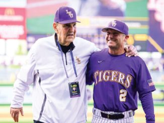 LSU Tigers baseball coach and player pose together on the field, with the player wearing a purple jersey that reads TIGERS and number 2
