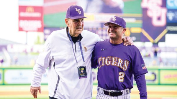 LSU Tigers baseball coach and player pose together on the field, with the player wearing a purple jersey that reads TIGERS and number 2