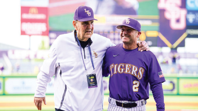 LSU Tigers baseball coach and player pose together on the field, with the player wearing a purple jersey that reads TIGERS and number 2