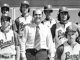 Black-and-white photo of a baseball team posing with their coach in a shirt and tie; players wear matching uniforms with B logos.