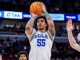 UCLA player in white jersey number 55 shoots a basketball over defenders during a game.