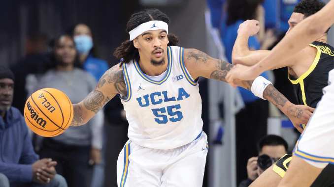 UCLA player wearing white jersey #55 dribbles the basketball during a game with defenders nearby.