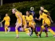 Group of LSU women's soccer players in yellow uniforms cheer and run on the field at night under stadium lights.